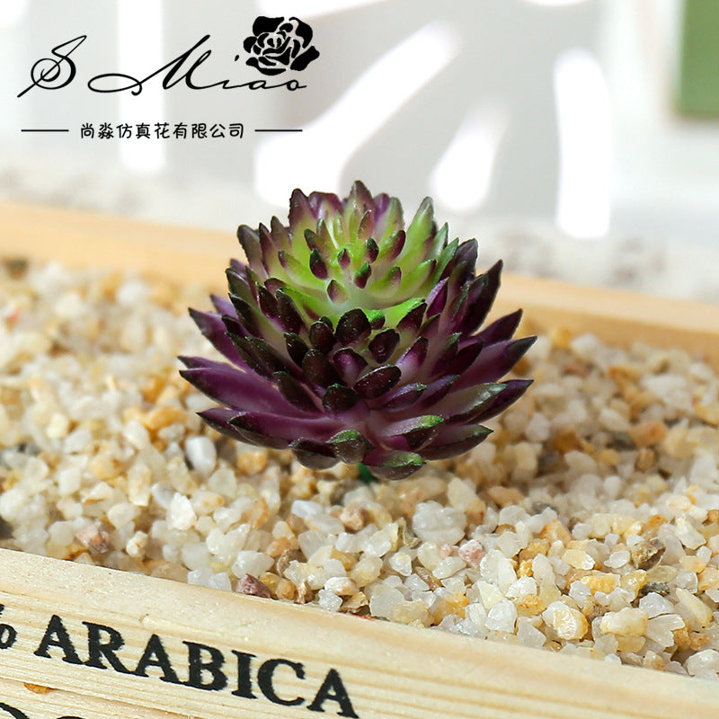 A small, dark purple artificial succulent bonsai ball is displayed on a wooden tray filled with light-colored gravel.