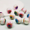 Un ensemble de dix perles de séparateur d'yeux en acrylique irisées avec des motifs colorés détaillés, éparpillées sur une su