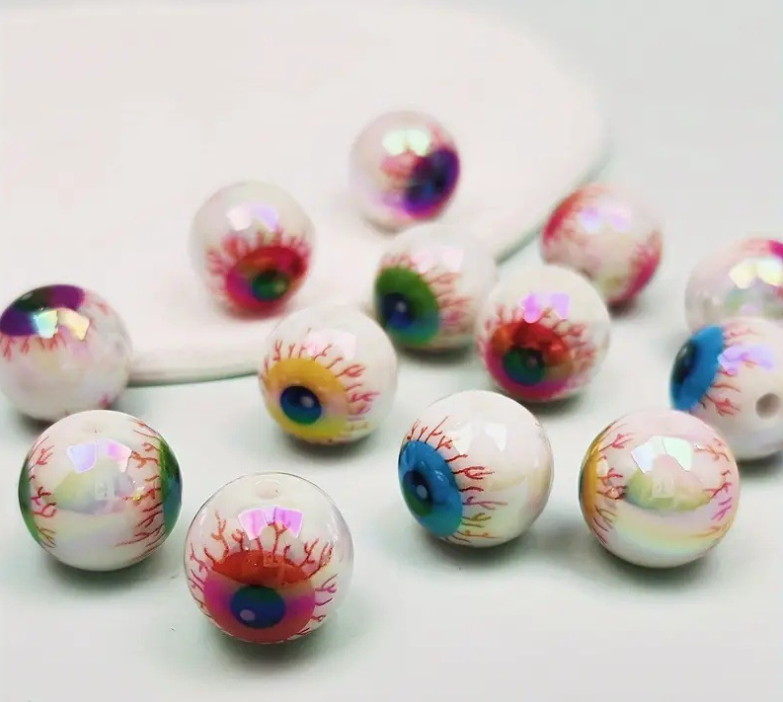 Un ensemble de dix perles de séparateur d'yeux en acrylique irisées avec des motifs colorés détaillés, éparpillées sur une su