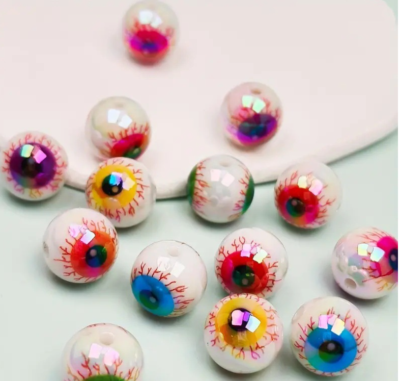 Un ensemble de dix perles de spacers oculaires en acrylique irisées avec des designs colorés et détaillés, éparpillées sur un