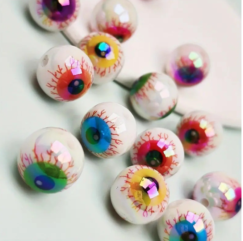 Un set de dix perles à séparateur d'yeux en acrylique iridescent avec des designs colorés et détaillés, éparpillées sur une s