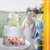 A wedding couple is pictured next to a tiered cake display featuring pink roses and white flowers.