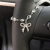 A silver rhinestone bow cross pendant necklace worn on a person's wrist, set against a dark car interior.