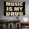 Black tapestry with white text that reads Music Is My Drug hanging above a wooden table.