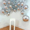A display of twelve metallic silver foil balloons hanging on a wall.