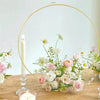 Ten gold metal hoop centerpieces with stands featuring white and pink flowers on a wooden table.