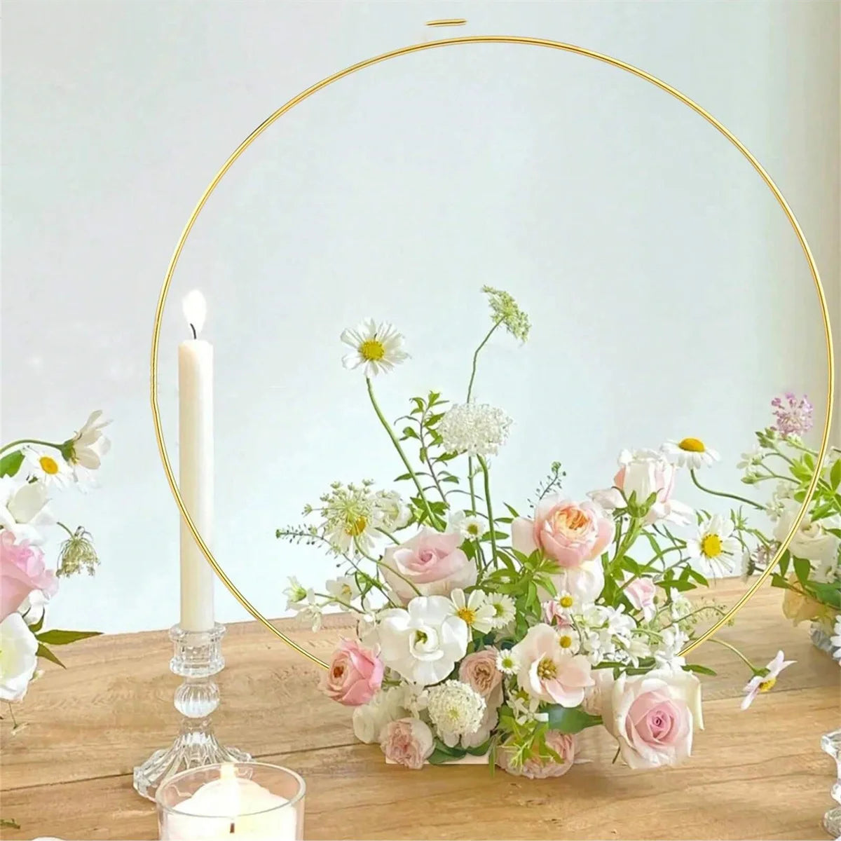 Ten gold metal hoop centerpieces with stands featuring white and pink flowers on a wooden table.