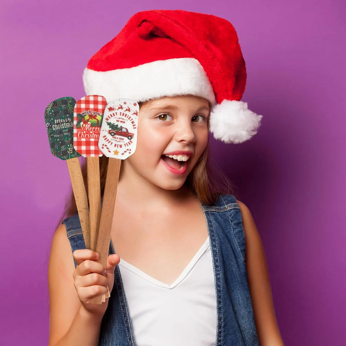 A smiling girl wearing a red and white Santa hat holds a set of festive Christmas silicone spatulas with wooden handles.