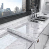 A stainless steel kitchen sink and faucet are installed in a white marble countertop, with a roll of marble self-adhesive wal