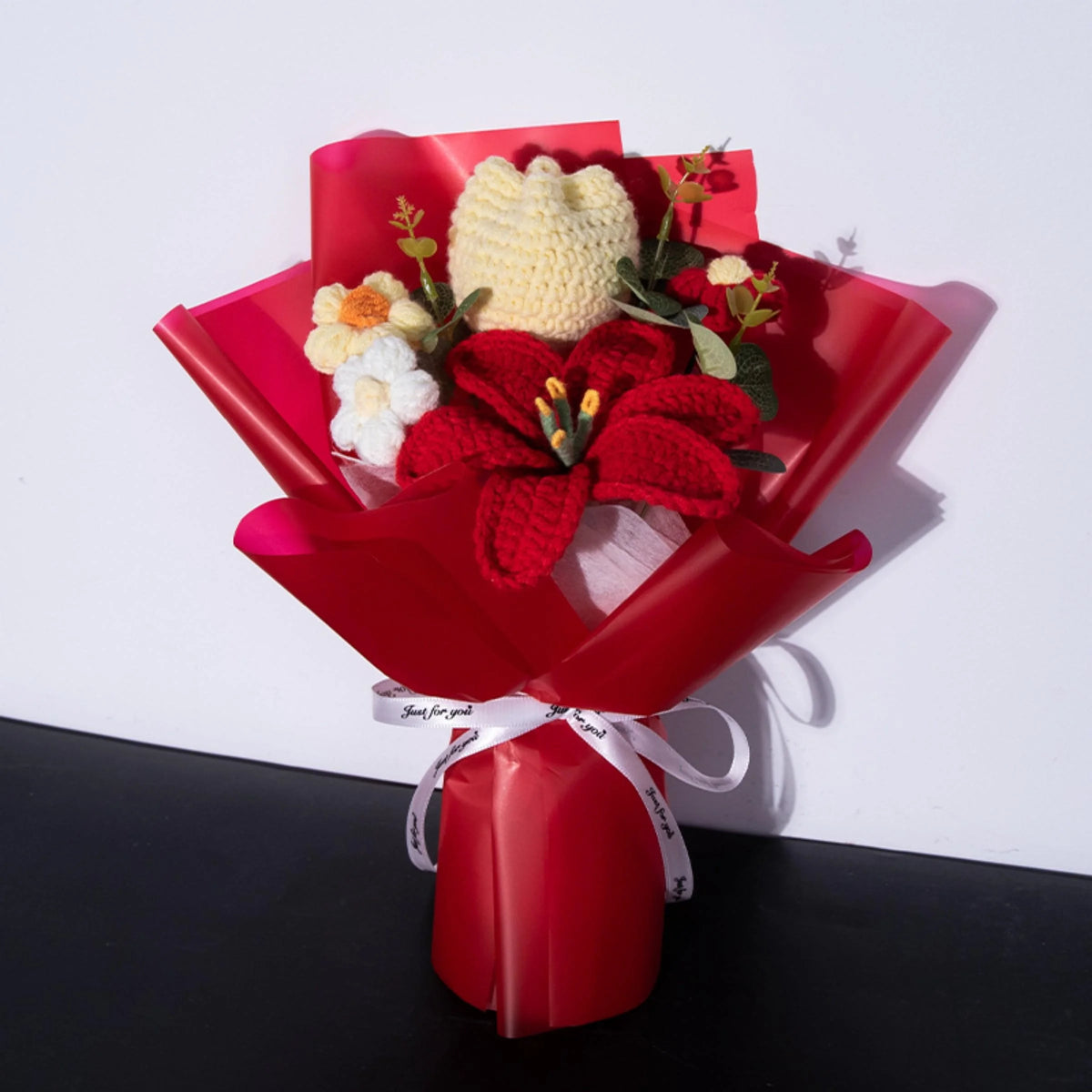 A bouquet of handmade crochet yarn flowers in yellow and red nestled in a red gift paper.