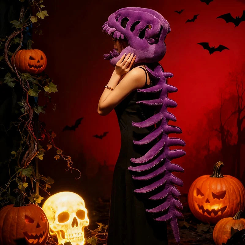 Un jouet en peluche violet en forme de squelette de dinosaure se tient sur un fond rouge foncé avec des accessoires d'Hallowe