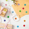 A flat lay of round expression stickers in various colors scattered on a white surface with wrapped gift boxes.