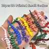 A hand holds 20 pieces of 3D printed small geckos in various colors and textures.