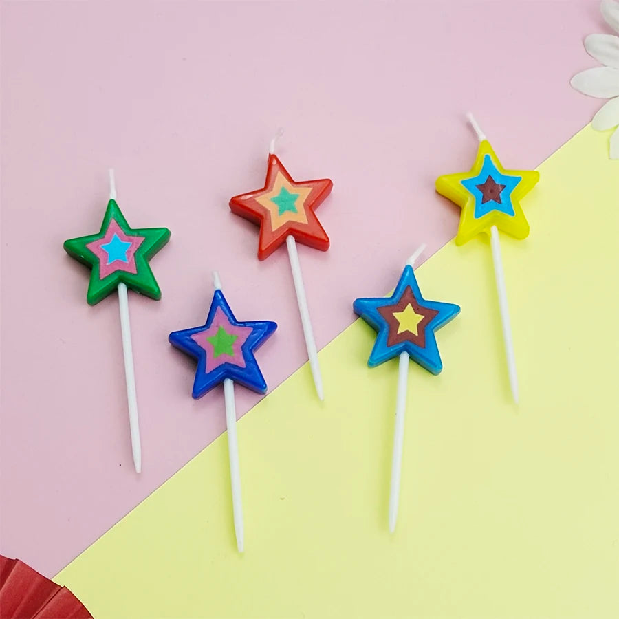 Several colorful star-shaped birthday cake candles in red, yellow, green, and blue are arranged on a pink and yellow backgrou
