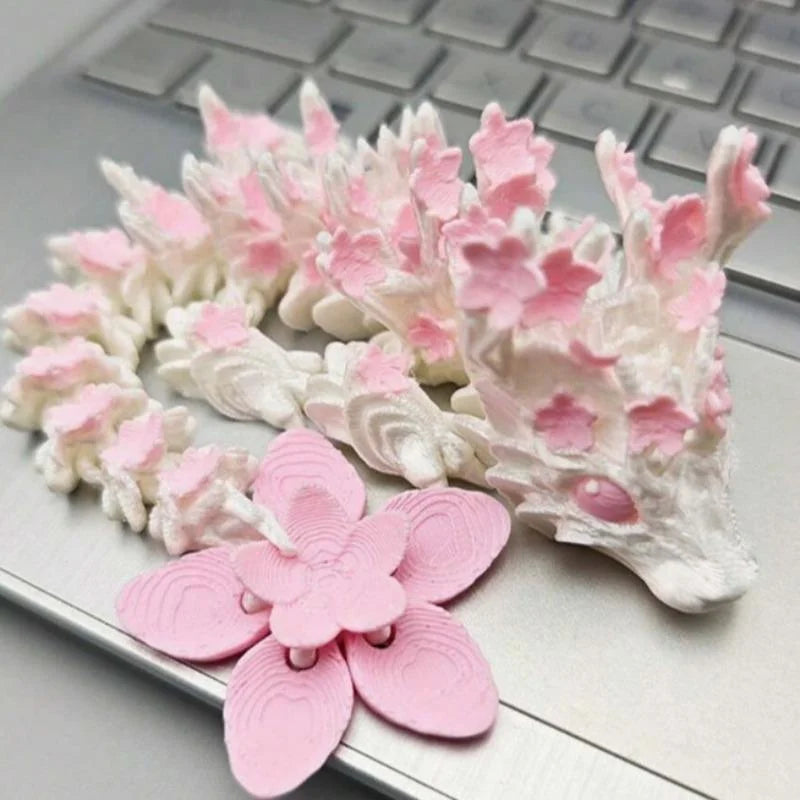 A miniature figurine of a dragon made from pink and white textured material, featuring a large pink cherry blossom flower.