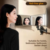 A woman is looking at a wall-mounted 3-sided folding mirror used for hair cutting or grooming.