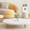 A white marble coffee table with a floral arrangement sits in front of a mustard yellow sofa.
