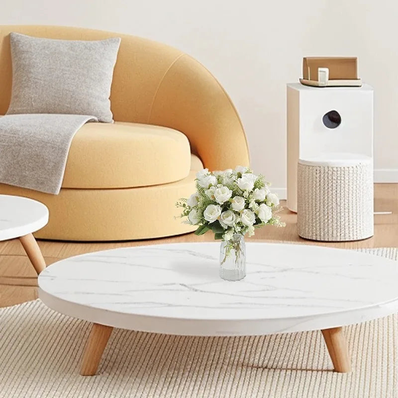 A white marble coffee table with a floral arrangement sits in front of a mustard yellow sofa.