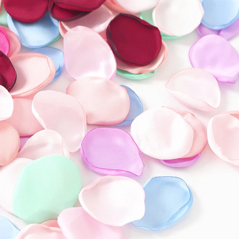 Una colección de pétalos de flores de seda artificial en tonos rosa, púrpura y azul, esparcidos sobre un fondo blanco.