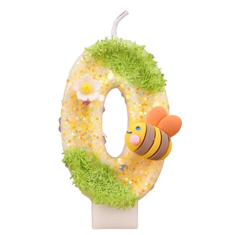 A yellow birthday candle shaped like the number 0 covered in green moss and featuring a bee decoration.