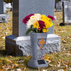 A gray solar LED cross memorial vase placed on a stone grave marker in a cemetery.