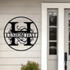 A black metal initial sign with custom text is mounted on a white clapboard siding next to a white door frame.