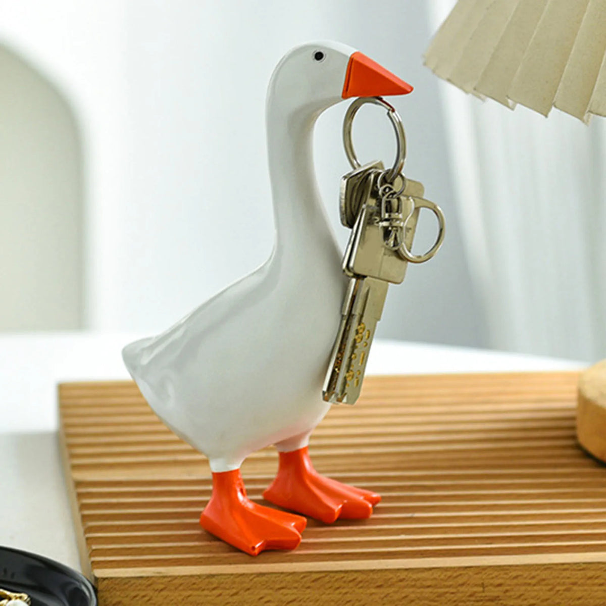 A white resin goose duck figurine with orange feet and a metal key holder attached.