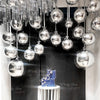 A display of metallic silver foil balloons hanging from a ceiling, set against a dark background.