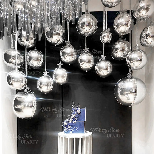 A display of metallic silver foil balloons hanging from a ceiling, set against a dark background.