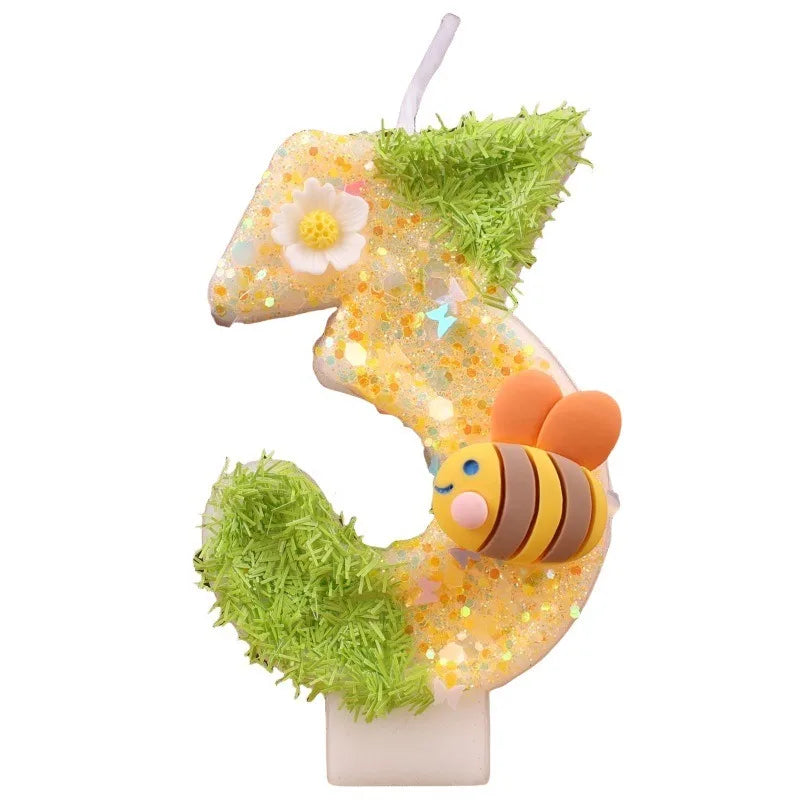 A birthday candle kit shaped like a bee, covered in gold sequins and green foliage.