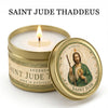 A gold tin candle labeled Saint Jude Thaddeus with a lit wick and a decorative label featuring the saint.