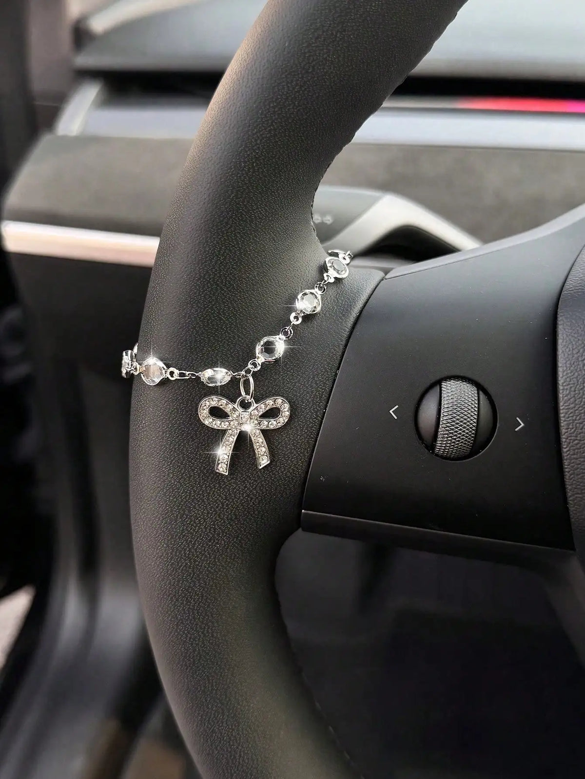 A luxury rhinestone bow cross pendant necklace is displayed on a car steering wheel.