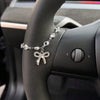A luxury rhinestone bow cross pendant necklace is displayed on a car steering wheel.