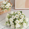 A bouquet of white silk touch artificial roses with green foliage displayed on a glass surface.