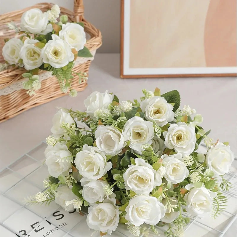 A bouquet of white silk touch artificial roses with green foliage displayed on a glass surface.