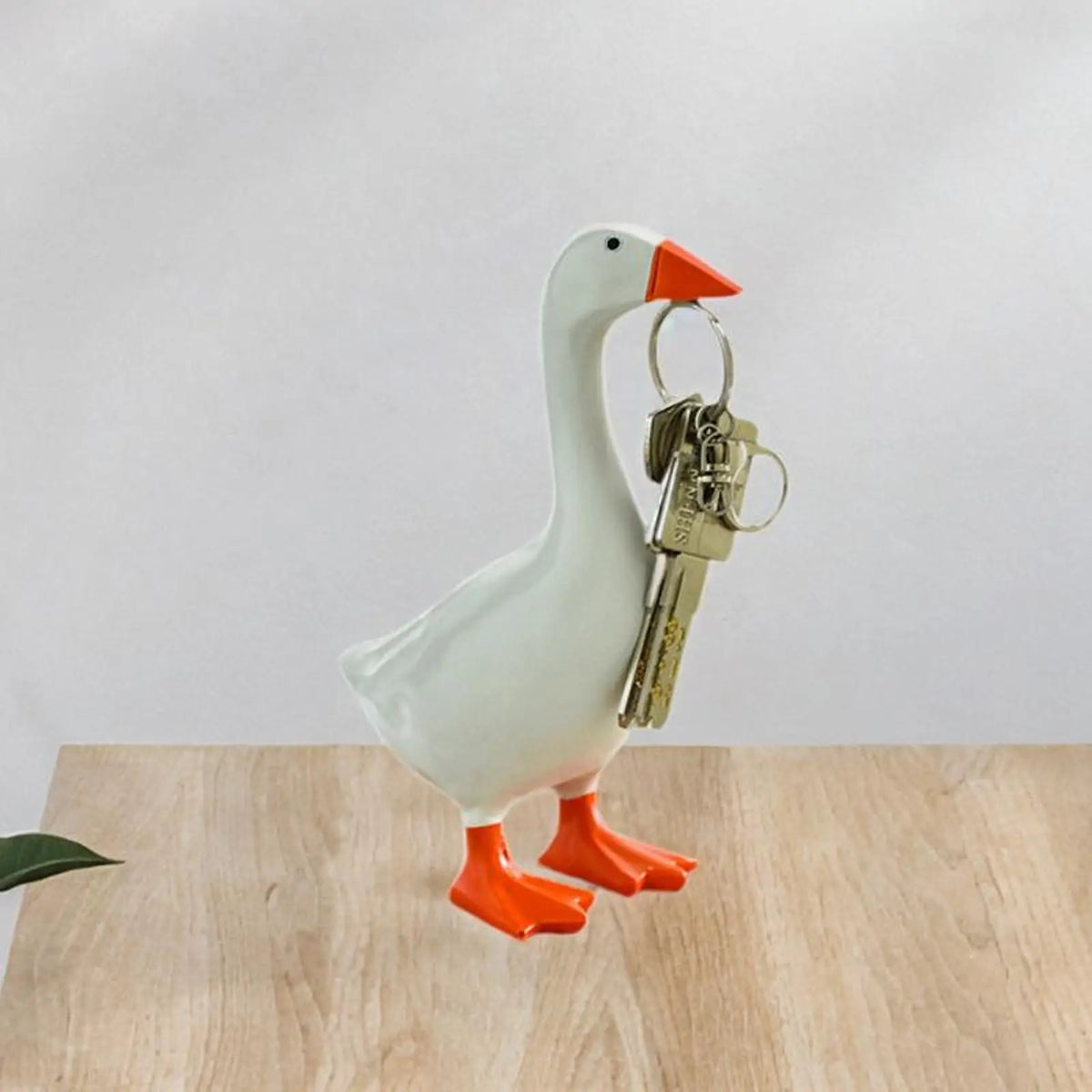 A white resin goose duck key holder decoration with orange feet and beak, displayed on a wooden surface.