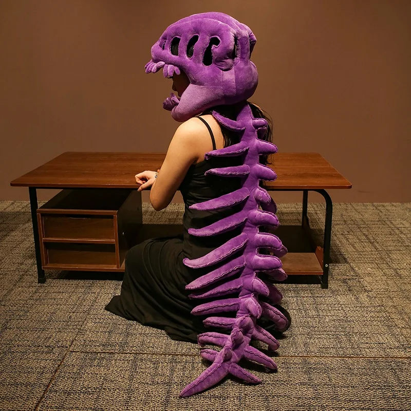 Peluche squelette de dinosaure réaliste violet à côté d'un bureau en bois.