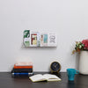 A clear acrylic floating shelf displaying several books against a white wall.