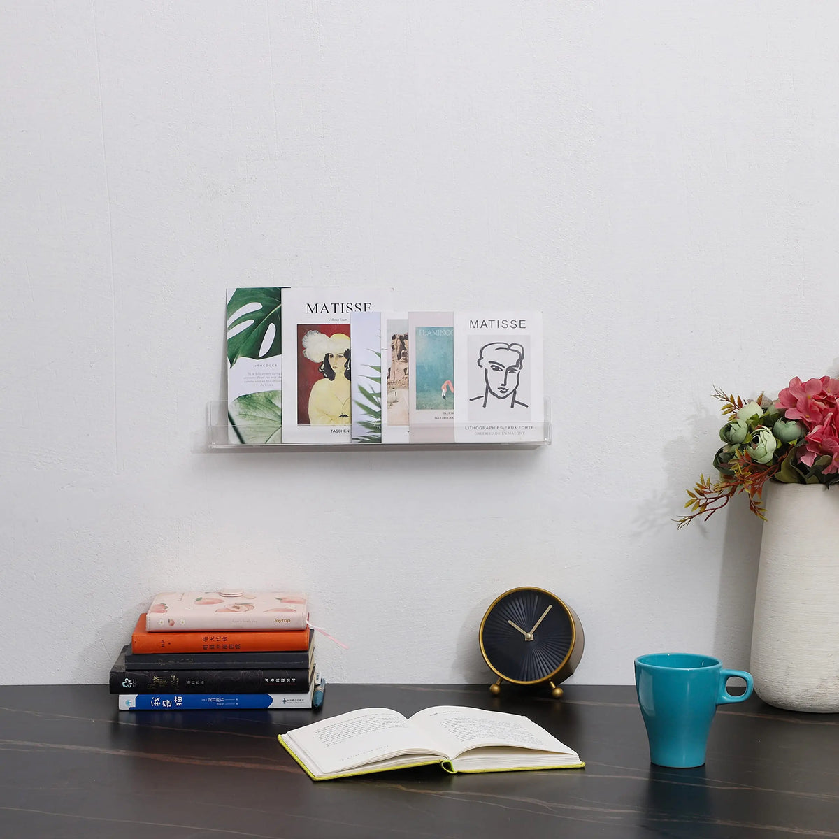 A clear acrylic floating shelf displaying several books against a white wall.