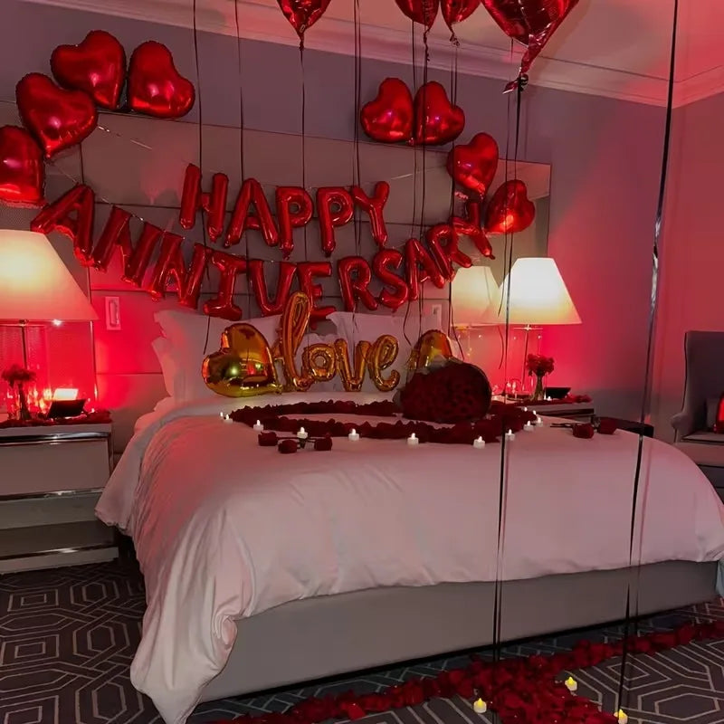 A bedroom decorated with red and gold heart decor, including a large hanging sign and red rose petals on the floor.