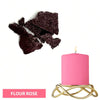 A pink candle in a gold wire holder next to dark purple flower rose dye blocks.