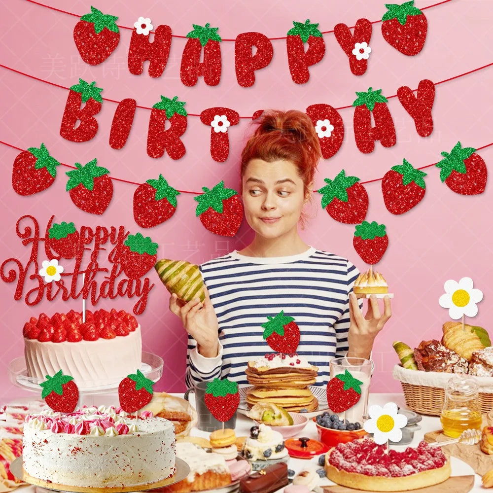 A festive birthday banner with strawberries and the words HAPPY BIRTHDAY, surrounded by various strawberry-themed party suppl