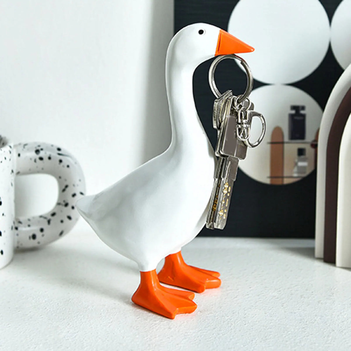 A white ceramic goose duck figurine with orange feet and a silver key holder attached.