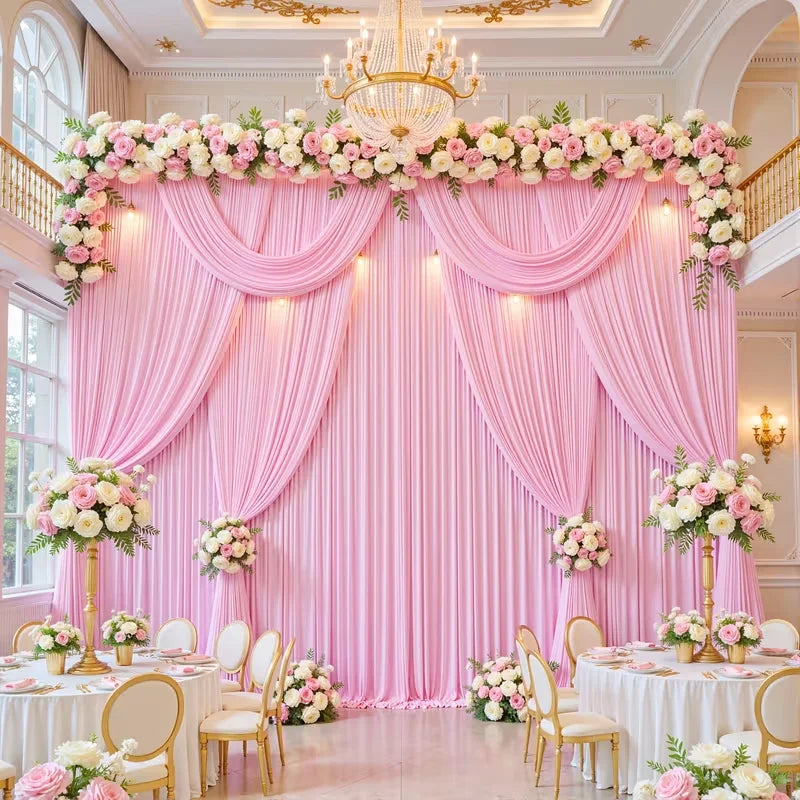 A pink draped backdrop with floral garlands and a golden chandelier for a wedding or event setting.