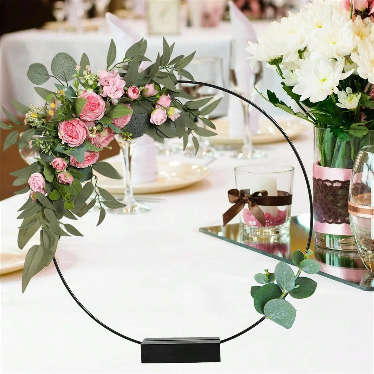 A black metal hoop centerpiece with pink roses and greenery on a white tablecloth.