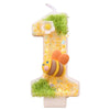 A golden number one candle decorated with green moss and a bee figure