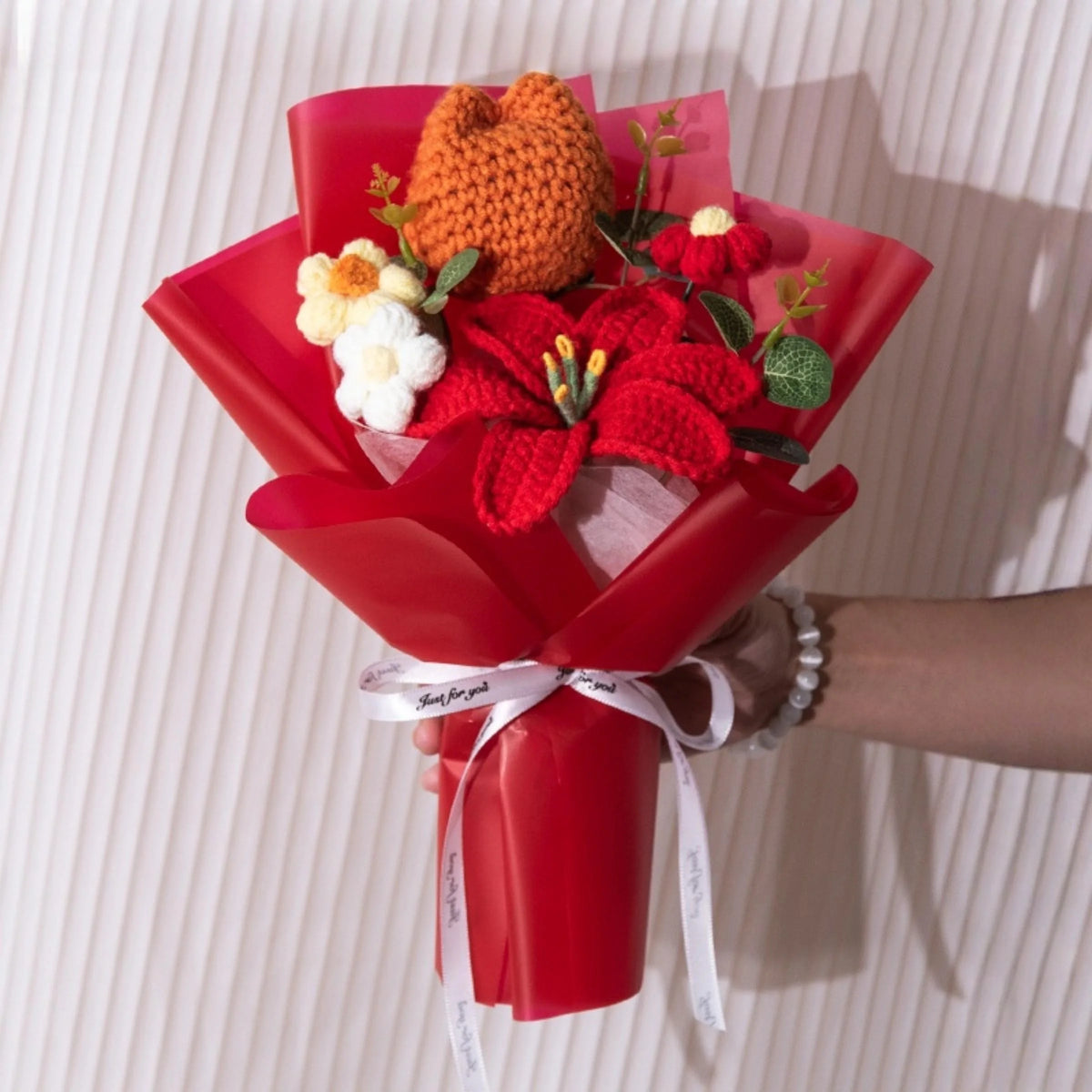 A bouquet of handmade crochet yarn flowers in orange and red nestled in a red paper wrapping.