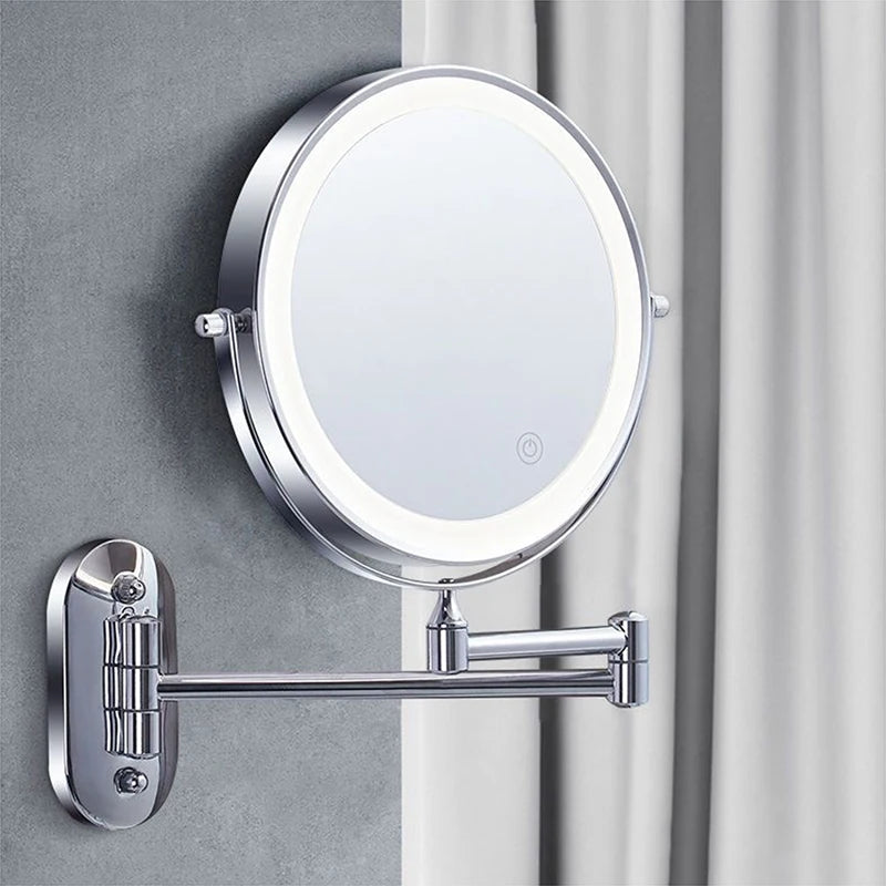 A round illuminated magnifying makeup mirror with a silver mounting bracket attached to a gray wall.