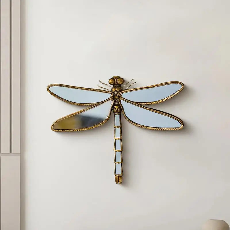 Miroir mural de libellule or avec des ailes translucides et un long pied sur un mur blanc.