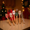 Five festive Christmas silicone spatulas with wooden handles arranged on a light surface.